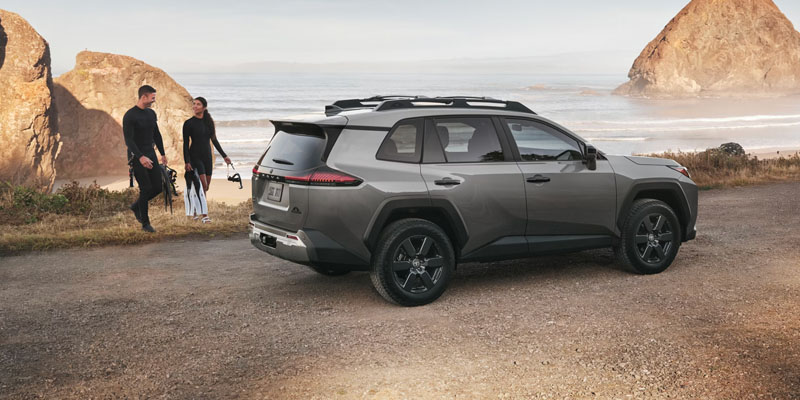 SUV parked near a rocky beach with two people standing beside it holding outdoor gear.